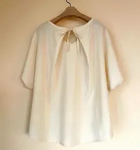 背中にキーホールとリボンが特徴の白トップス。ゆったりAラインで女性らしい印象です。